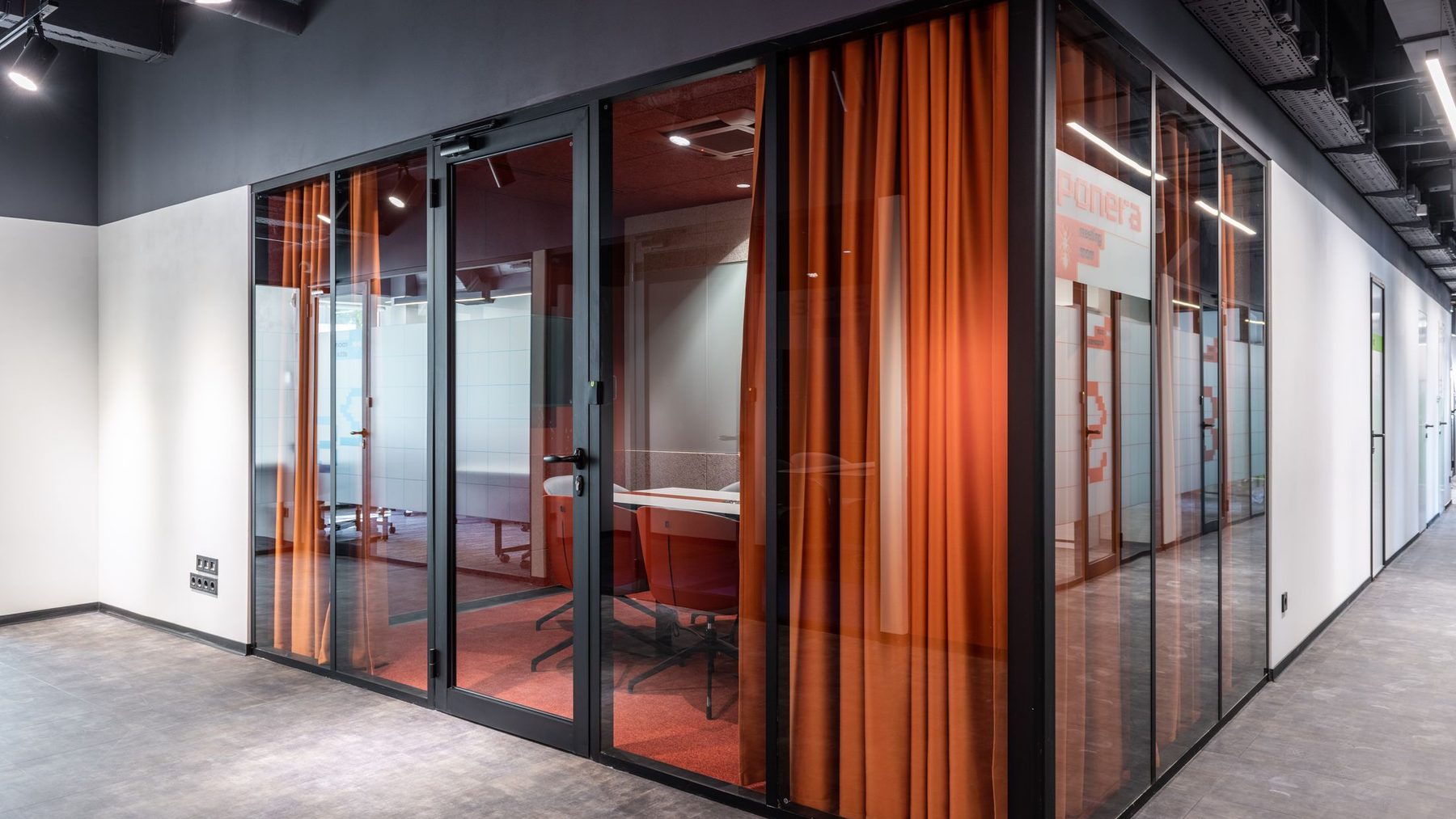 A modern office corridor lined with glass-walled meeting rooms